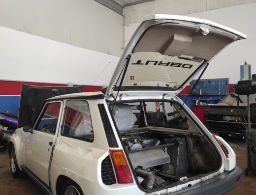Renault 5 Turbo bianca con cofano e bagagliaio aperti in un garage, dettaglio del motore posteriore. Auto d'epoca sportiva per appassionati di motori e tuning.