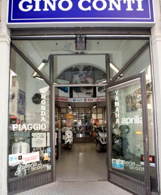 Ingresso del negozio Gino Conti, rivenditore autorizzato Piaggio, Aprilia, Vespa, Honda e Yamaha. Vetrina con scooter e moto in esposizione. Servizi di vendita e assistenza per motocicli.