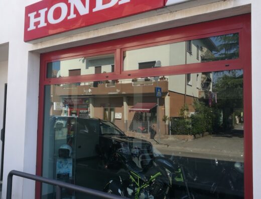 Concessionario Honda con vetrina che espone una moto Kawasaki Z900 verde e nera, accessori moto e riflessi della strada e degli edifici circostanti.