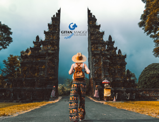 Una viaggiatrice con zaino e cappello di paglia si avvicina a un cancello balinese. Gitan Viaggi Trento, viaggi su misura.