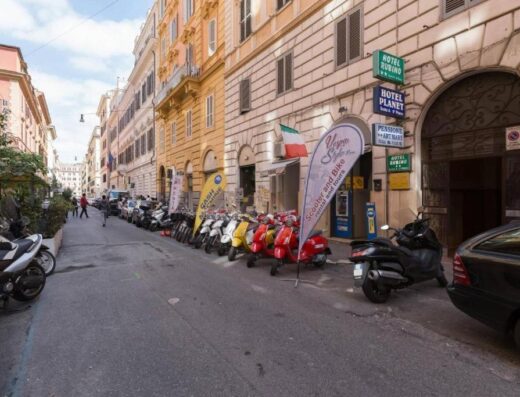 File di moto e scooter Vespa colorati parcheggiati su una strada di Roma vicino a un servizio di noleggio moto e viaggi in Italia.