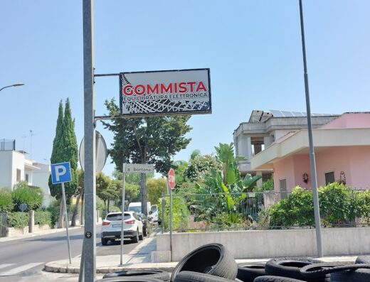 Cartello stradale del gommista da Sergio Mauro con pneumatici impilati in primo piano, offre servizi di equilibratura elettronica per moto e auto