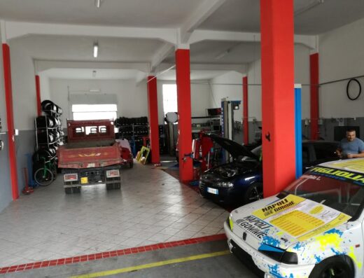Interno di un'officina gommista a Napoli, Baronissi, con auto in riparazione, scaffali di pneumatici e attrezzature per la sostituzione gomme.