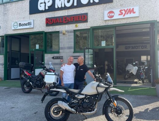 Foto di due uomini davanti a GP Motor Snc, concessionaria moto con marchi Benelli, Royal Enfield e SYM. In primo piano una moto adventure e in secondo piano una moto da turismo.