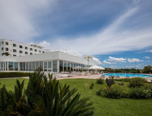 Grand Hotel Costa Brada exterior view showcasing the building, pool, and well-manicured green spaces under a partly cloudy sky.
