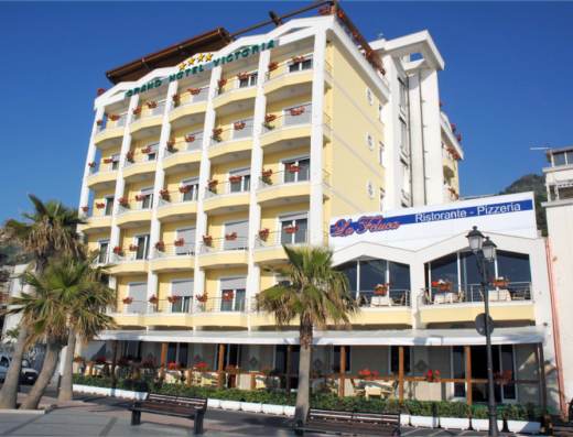 Grand Hotel Victoria a Maiori, Costiera Amalfitana, con ristorante-pizzeria La Feluca. Hotel a quattro stelle con balconi fioriti, palme e vista mare. Servizi di lusso per viaggiatori.