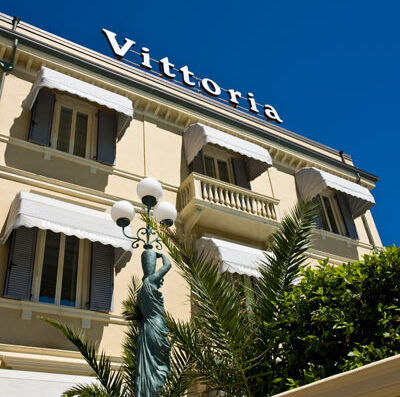 Grand Hotel Vittoria, Viale Gorizia, Pesaro. Facciata dell'hotel con una statua di donna con un vaso sulla testa e palme.