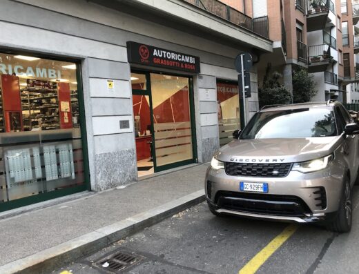Image of a Land Rover Discovery parked in front of Autoricambi Grassotti & Rosa, an auto parts store. The store's windows display various car parts and accessories.