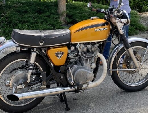 Graziano Ferrini's restored yellow Honda CB450 motorcycle, a vintage bike with a black racing stripe, parked outdoors.