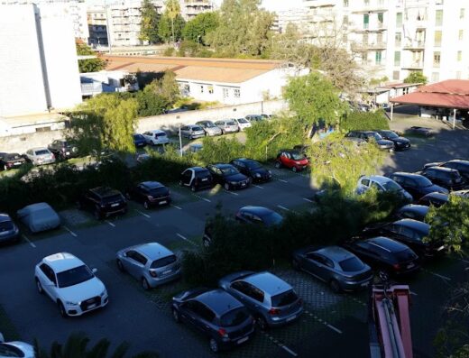 Vista aerea del Green Parking Catania Parcheggio 24H con auto parcheggiate, alberi, edifici circostanti e segnaletica orizzontale.