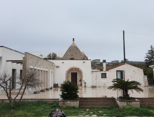 Grotta Cilicia: Tipica costruzione pugliese con tetto a cono in pietra, pareti bianche e vegetazione circostante, architettura tradizionale della Puglia.