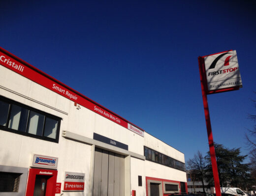 Esterno dell'officina Gruppo Brusamarello a Padova, specializzata in servizi per auto e moto, con insegne di First Stop, Bridgestone e Firestone. Servizi di riparazione cristalli e smart repair.