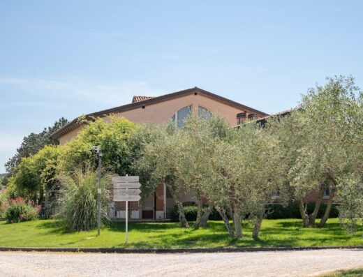 Guadalupe Tuscany Resort view featuring the building's facade, olive trees, green lawn, and a directional signpost under a clear blue sky.