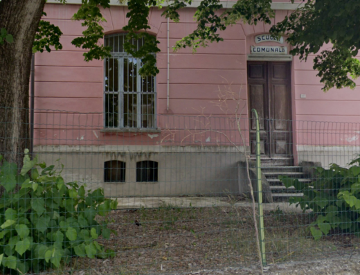 Fotografia di un edificio rosa con la scritta "Scuola Comunale" sopra la porta d'ingresso, circondato da alberi e vegetazione, in Piemonte.