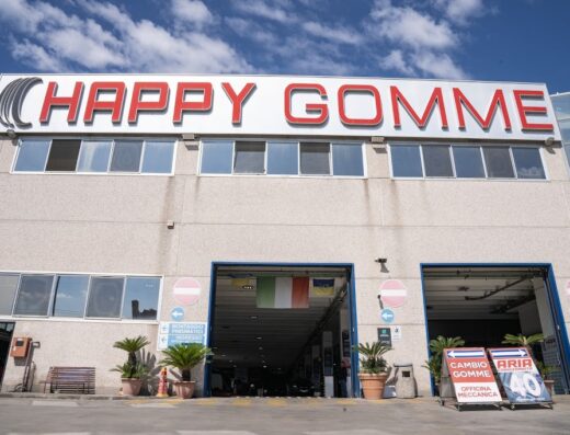 Foto dell'esterno di Happy Gomme a Pomigliano, specialista in pneumatici e servizi per auto e moto. Insegna rossa ben visibile e bandiere italiana e ucraina.