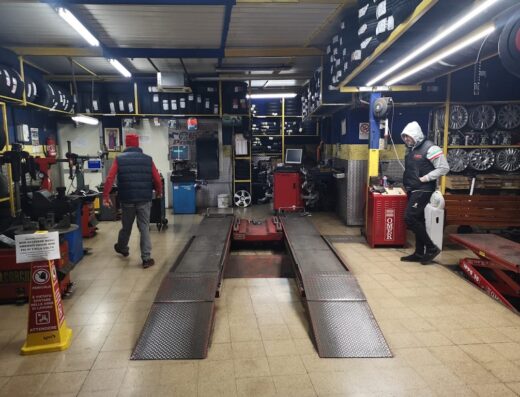 Interno dell'officina Happy Gomme a Sorrento, con ponte sollevatore, scaffali di pneumatici e cerchi, e due clienti.