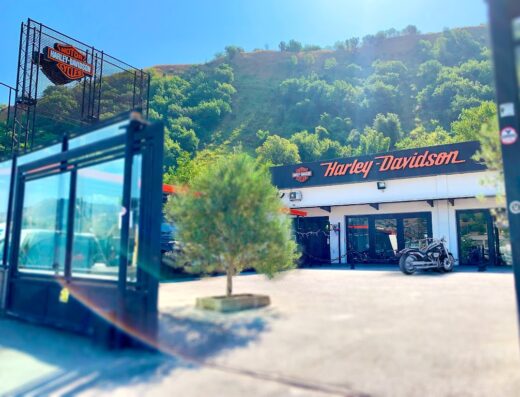 Harley-Davidson Napoli: Concessionaria con moto in esposizione, insegna Harley-Davidson e cartello pubblicitario, immersa nel paesaggio collinare napoletano.