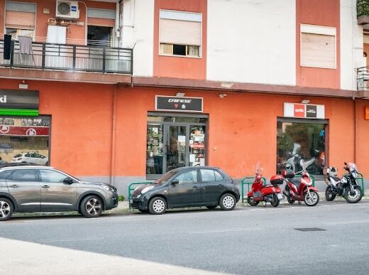 Foto della facciata di HD Motor Srl, rivenditore di moto Kawasaki, Dainese, Aprilia e KTM. Sono visibili moto parcheggiate e auto.