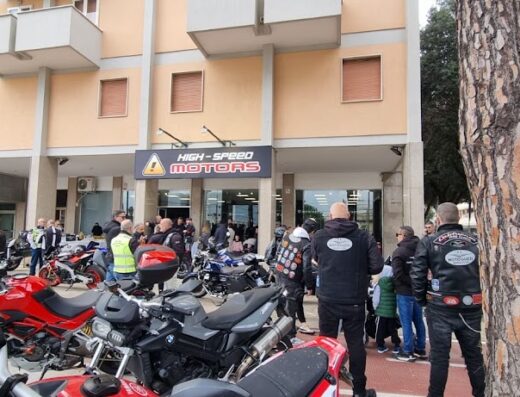 Affollato concessionario High-Speed Motors con motociclette parcheggiate e numerosi clienti di accessori e servizi moto