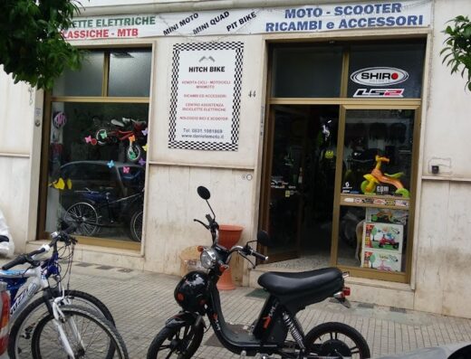 Negozio di moto e bici Hitch Bike con scooter elettrico parcheggiato di fronte, vendita e assistenza cicli, motocicli, ricambi e accessori