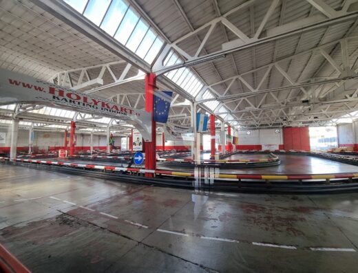 Pista di karting indoor presso Holykartroma, con curve segnalate e bandiere decorative, ideale per appassionati di motorsport e attività di svago al chiuso.