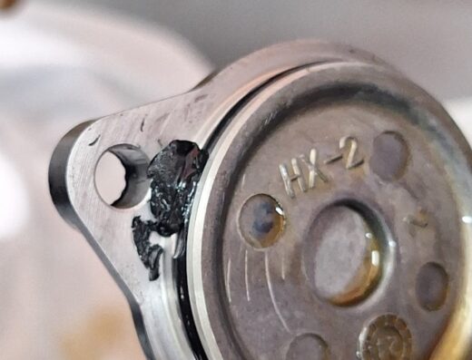 Dettaglio di un componente del motore di una moto Honda, con la sigla HX-2 visibile, probabilmente in un'officina a Cagliari. Mostra segni di usura e manutenzione.