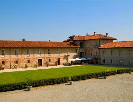Hotel Antico Podere Propano vista esterna con prato verde curato, ombrelloni bianchi e tavoli per gli ospiti, ideale per un soggiorno rilassante in Italia