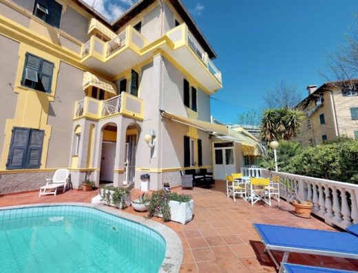 Hotel Arcobaleno: vista esterna dell'hotel con piscina, terrazza con lettini blu e tavoli gialli per il relax e il divertimento.