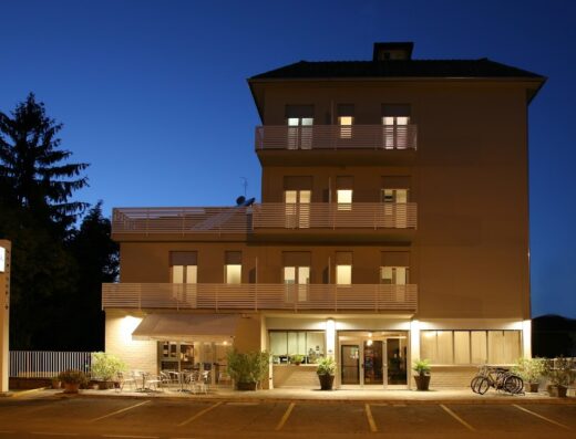 Hotel Astoria illuminato di notte, con balconi, tavolini esterni e biciclette parcheggiate di fronte, insegna visibile