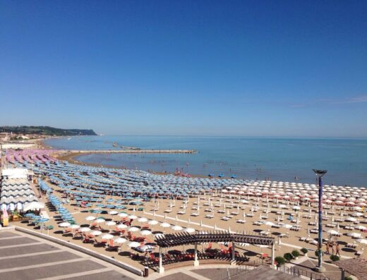 Vista panoramica della spiaggia di Fano dall'Hotel Astoria, con ombrelloni colorati, mare cristallino e cielo azzurro.