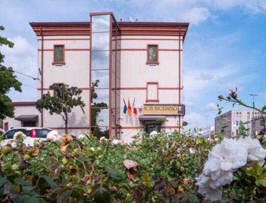 Hotel Autoespresso Venezia: facciata dell'hotel con rose bianche in primo piano, architettura moderna e bandiere decorative.