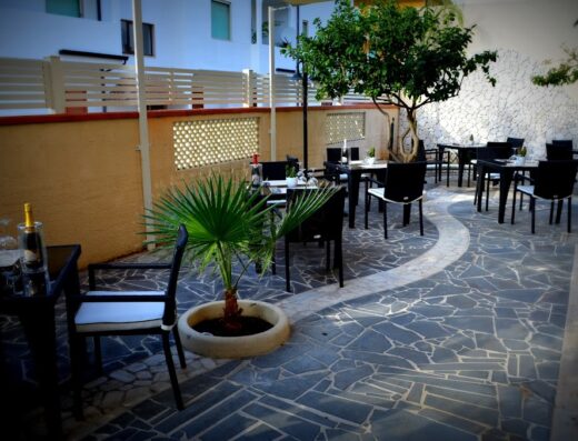 Cortile esterno dell'Hotel Barbieri con tavoli, sedie, pavimentazione in pietra e vegetazione, ideale per colazioni e cene all'aperto.