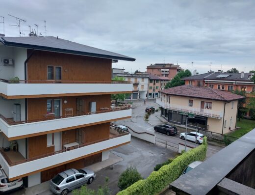 Vista esterna dell'Hotel Bella Venezia che mostra l'architettura circostante, con balconi, edifici residenziali e auto parcheggiate in strada.