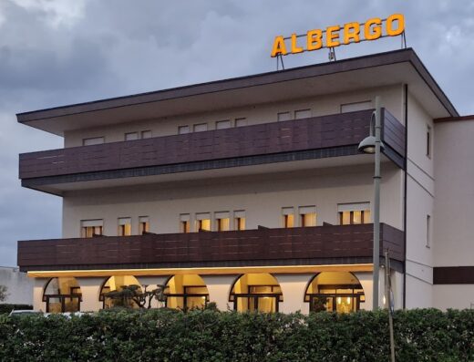 Hotel Belvedere: Facciata esterna dell'albergo a tre piani con balconi marroni e insegna luminosa arancione 'Albergo' sul tetto, situato in una zona tranquilla.