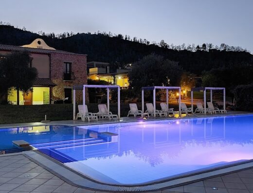 Hotel Cardedu: Vista serena della piscina illuminata di sera, con lettini sotto strutture ombreggiate e sullo sfondo la facciata dell'hotel.