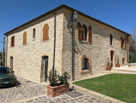 Hotel Castello di Septe exterior view showcasing the stone facade, arched windows with wooden shutters, manicured lawn, and a parked car.