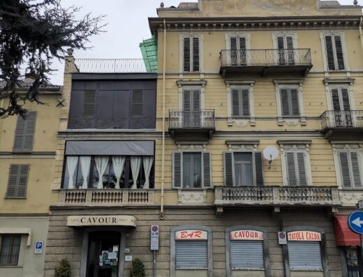 Facciata dell'Hotel Cavour, con ingresso principale, insegne di bar e tavola calda chiusi, balconi in ferro battuto e architettura storica.