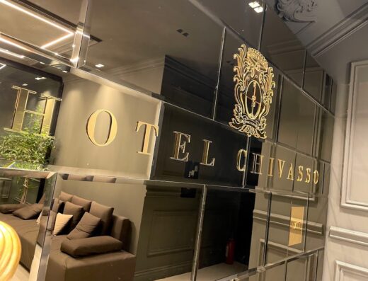 Hotel Chivasso ex Hotel Ritz: dettaglio dell'insegna dorata riflessa su una parete a specchi, con divano marrone in primo piano.