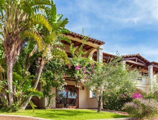 Esterno dell'Hotel Club Saraceno, con vegetazione lussureggiante, fiori colorati, balconi con archi e arredi da esterno.
