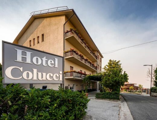 Hotel Colucci, a multi-story building with balconies adorned with flowers, as seen from the street with its sign.
