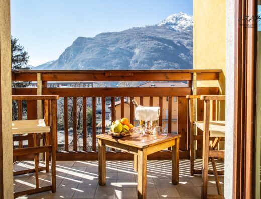 Balcone dell'Hotel Crabun con vista sulle montagne, tavolo con frutta fresca, champagne e calici per un soggiorno di lusso e relax.