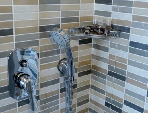 Dettaglio del bagno dell'Hotel Désirée con doccia, miscelatore cromato e mensola con prodotti da bagno, rivestimento in piastrelle mosaico.