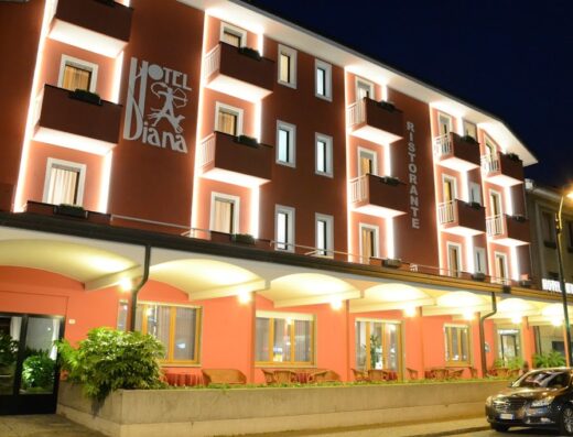 Facciata illuminata dell'Hotel Diana di notte, con balconi, ristorante e auto parcheggiata. Hotel Diana, accogliente e confortevole