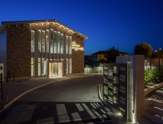 Dimora Del Monaco Hotel vista notturna con illuminazione, ingresso e cancello moderni, architettura elegante e cielo sereno.