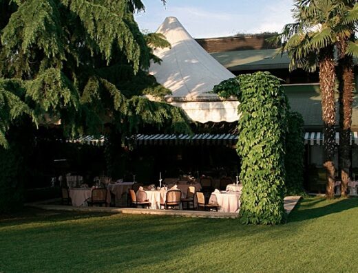 Verdeggiante giardino dell'Hotel Due Mori con tavoli apparecchiati sotto un tendone e vegetazione rigogliosa, ideale per eventi all'aperto e relax