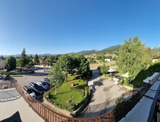 Vista panoramica dell'Hotel Edelweiss con parcheggio auto, giardini curati e montagne sullo sfondo, ideale per un soggiorno rilassante.