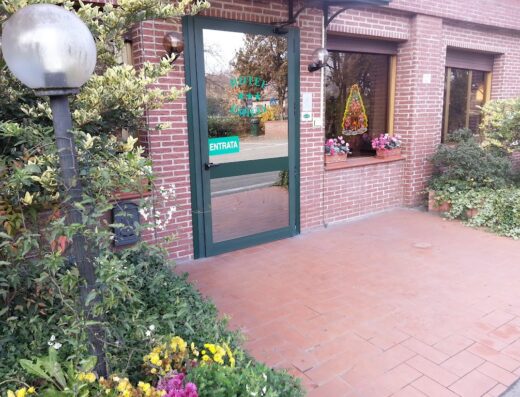 Ingresso dell'Hotel Emilia con porta a vetri verde e insegna "Entrata". Facciata in mattoni rossi, lampione sferico e decorazioni floreali.