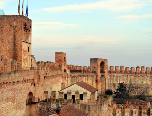 Veduta aerea delle mura medievali di Montagnana, Veneto, Italia, con torri merlate in mattoni rossi, bandiere e cielo sereno. Destinazione turistica e patrimonio storico.