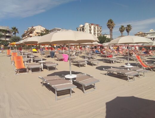 Spiaggia attrezzata presso Hotel Flora Alba Adriatica, con ombrelloni, lettini e sedie a sdraio disposti sulla sabbia fine.