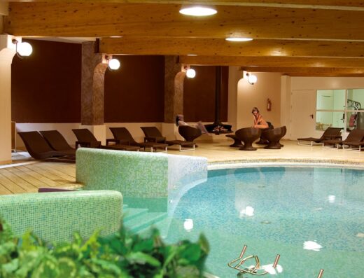 Interno dell'Hotel Giubileo con piscina interna, lettini prendisole e area relax con caminetto per un soggiorno all'insegna del benessere e del relax.